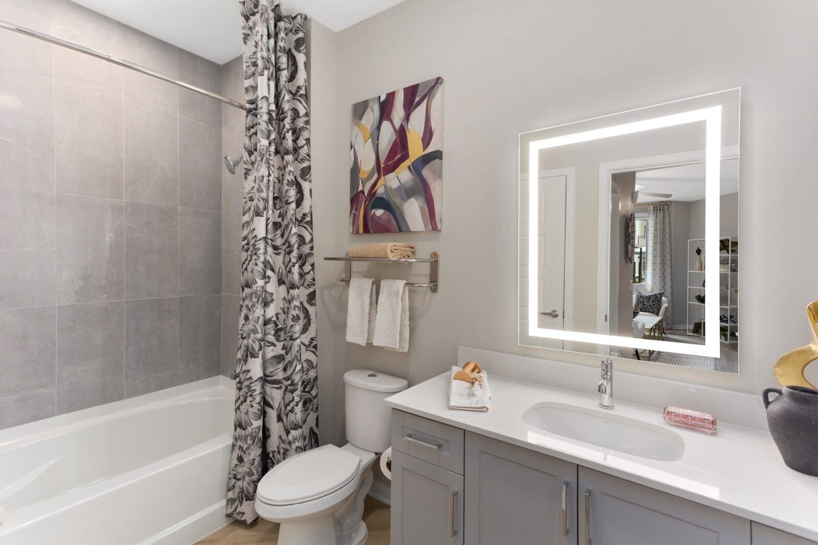 Modern bathroom with gray walls, vanity, and tub; a patterned shower curtain, and a lit mirror at Echo Biltmore in Phoenix, AZ..