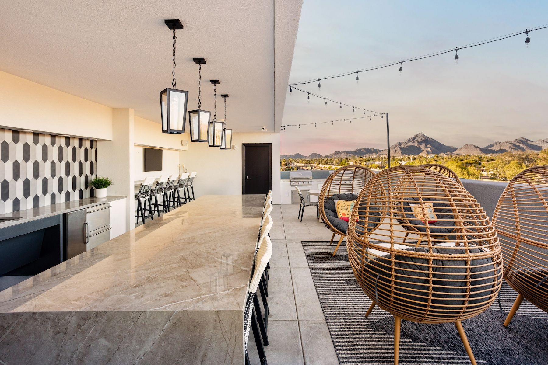 Rooftop bar with hanging lights, counter with stools, wicker chairs, and mountain views at Echo Biltmore in Phoenix, AZ..