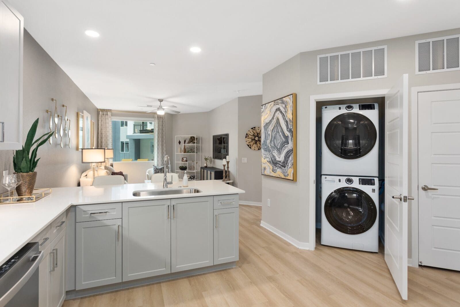 Modern kitchen with gray cabinets, stacked washer/dryer, and open living area with a balcony at Echo Biltmore in Phoenix, AZ..