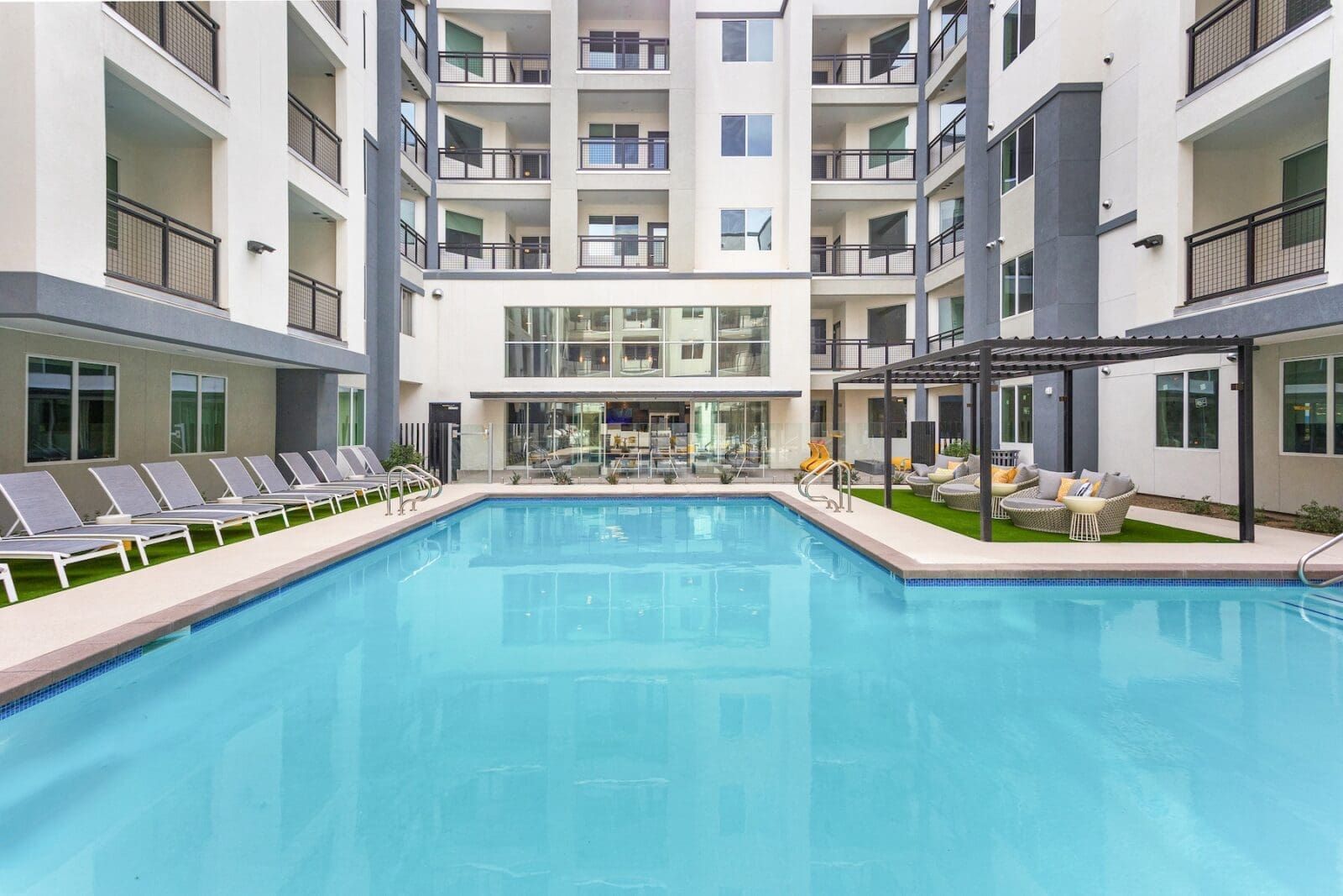 Swimming pool in an apartment complex courtyard, surrounded by lounge chairs and multi-story buildings at Echo Biltmore in Phoenix, AZ..