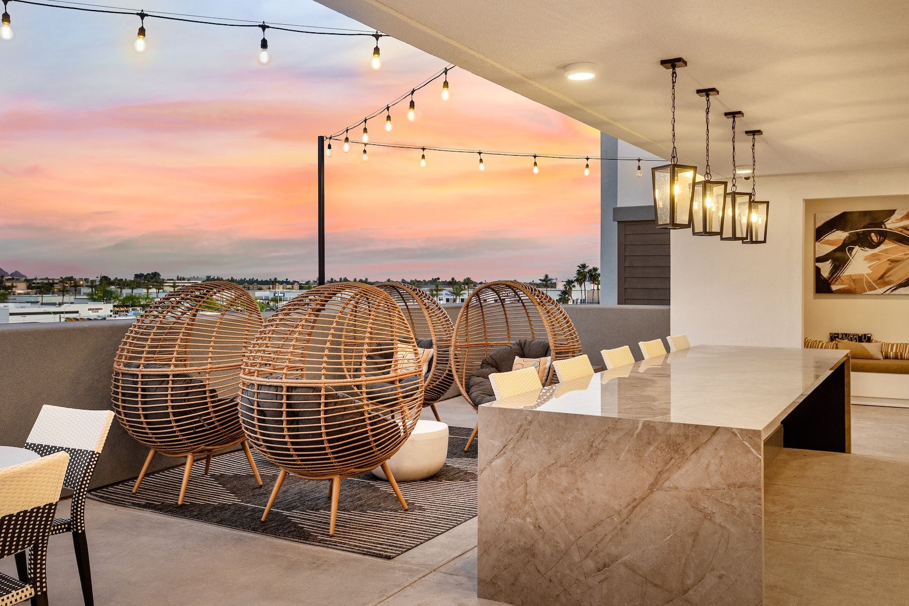 Rooftop patio at sunset with hanging lights, woven chairs, bar seating, and city view at Echo Biltmore in Phoenix, AZ..