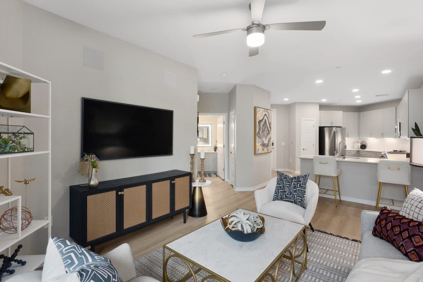 Living room with TV, open to kitchen. White furniture, light wood floors, neutral walls at Echo Biltmore in Phoenix, AZ..