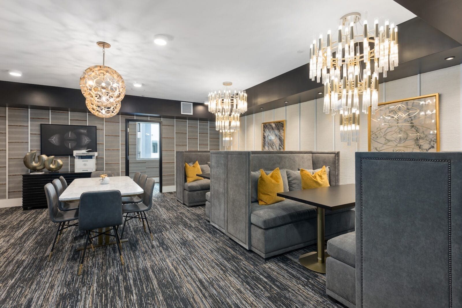 An elegant lounge area with chandeliers, booths, a table, and a textured patterned carpet at Echo Biltmore in Phoenix, AZ..
