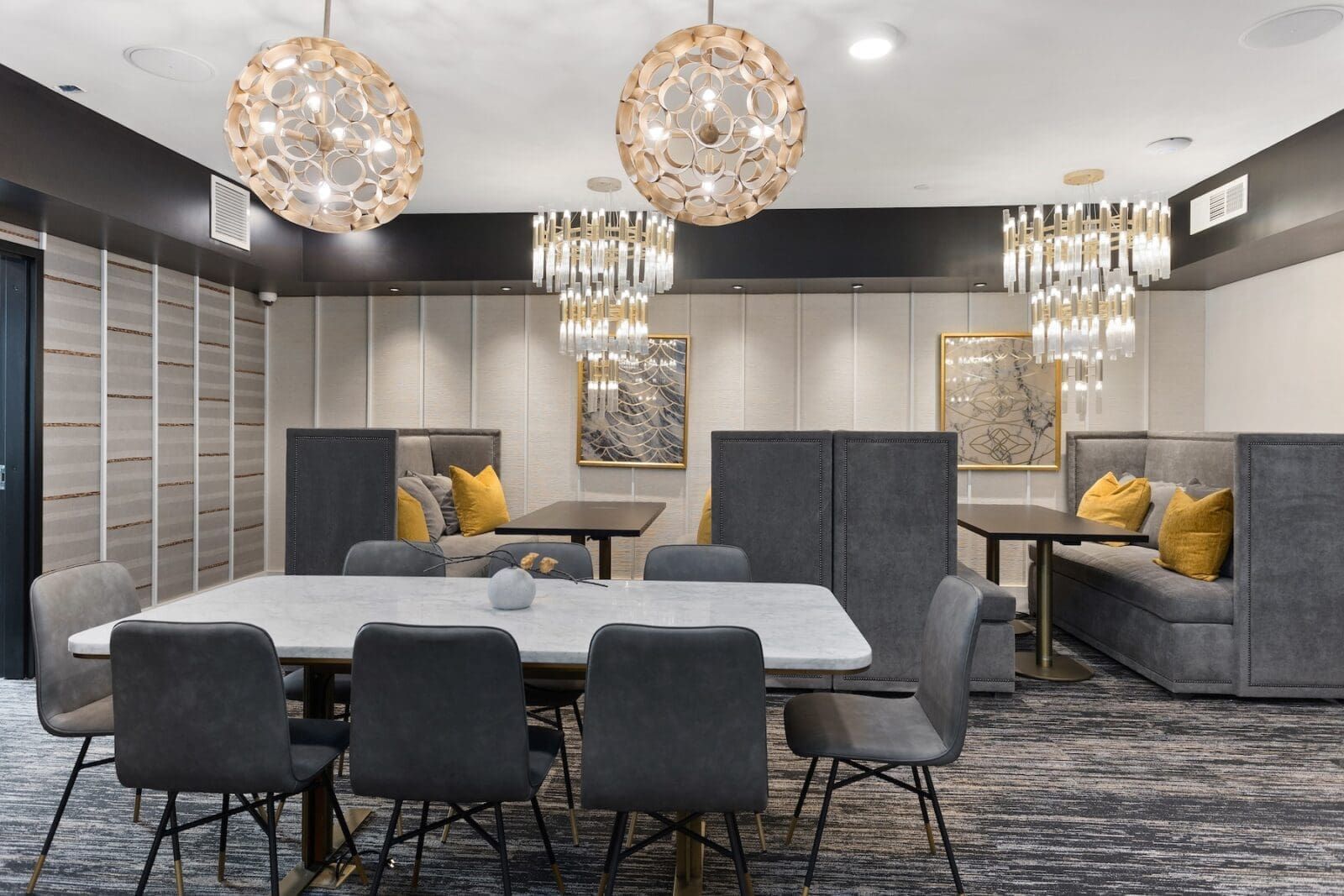 Restaurant dining area with gray chairs, tables, and booths. Gold chandeliers and wall art.