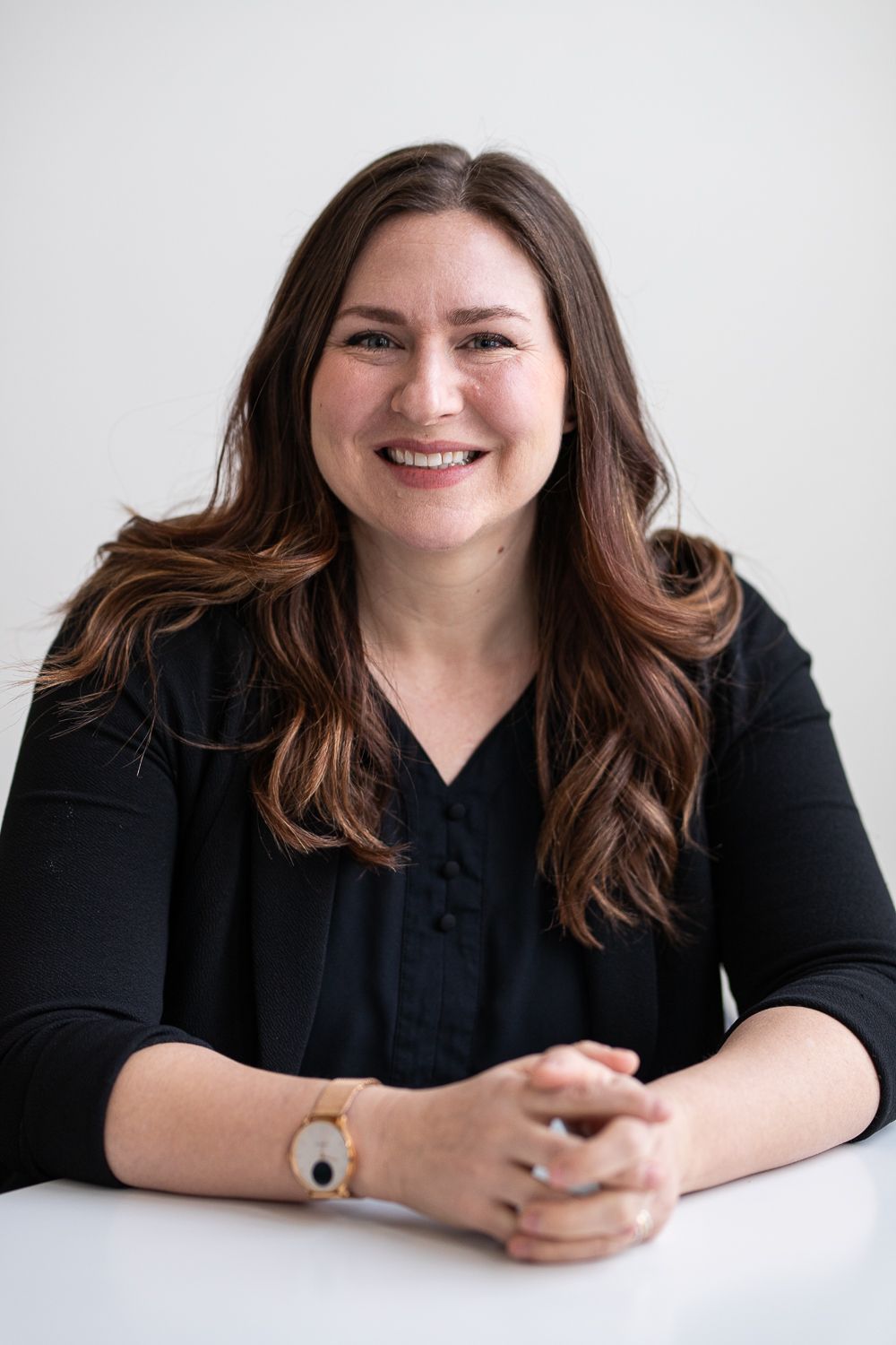 Woman with long brown hair, smiling, wearing a black sweater, sitting at a table.