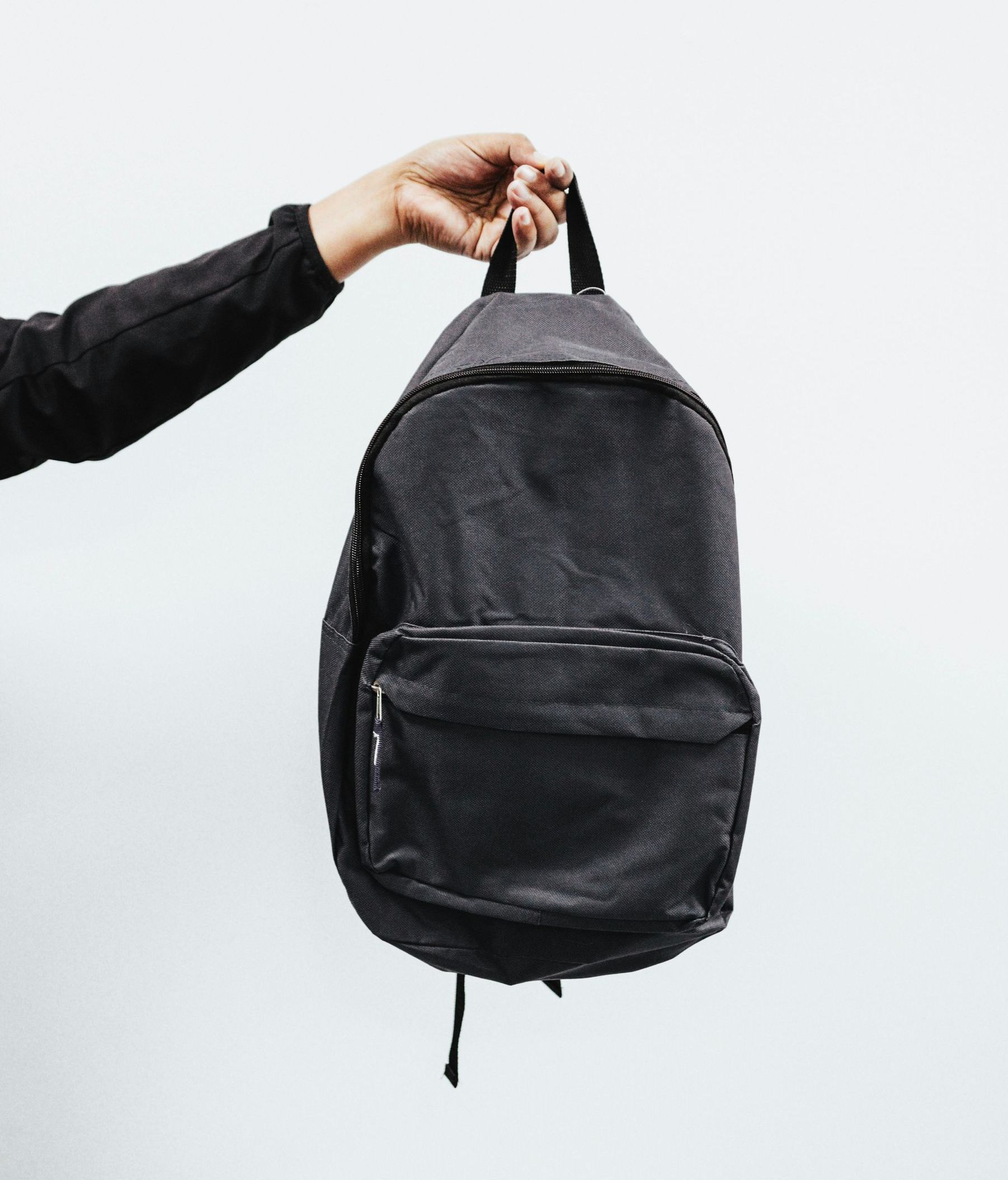 A hand holding a black backpack against a white background.