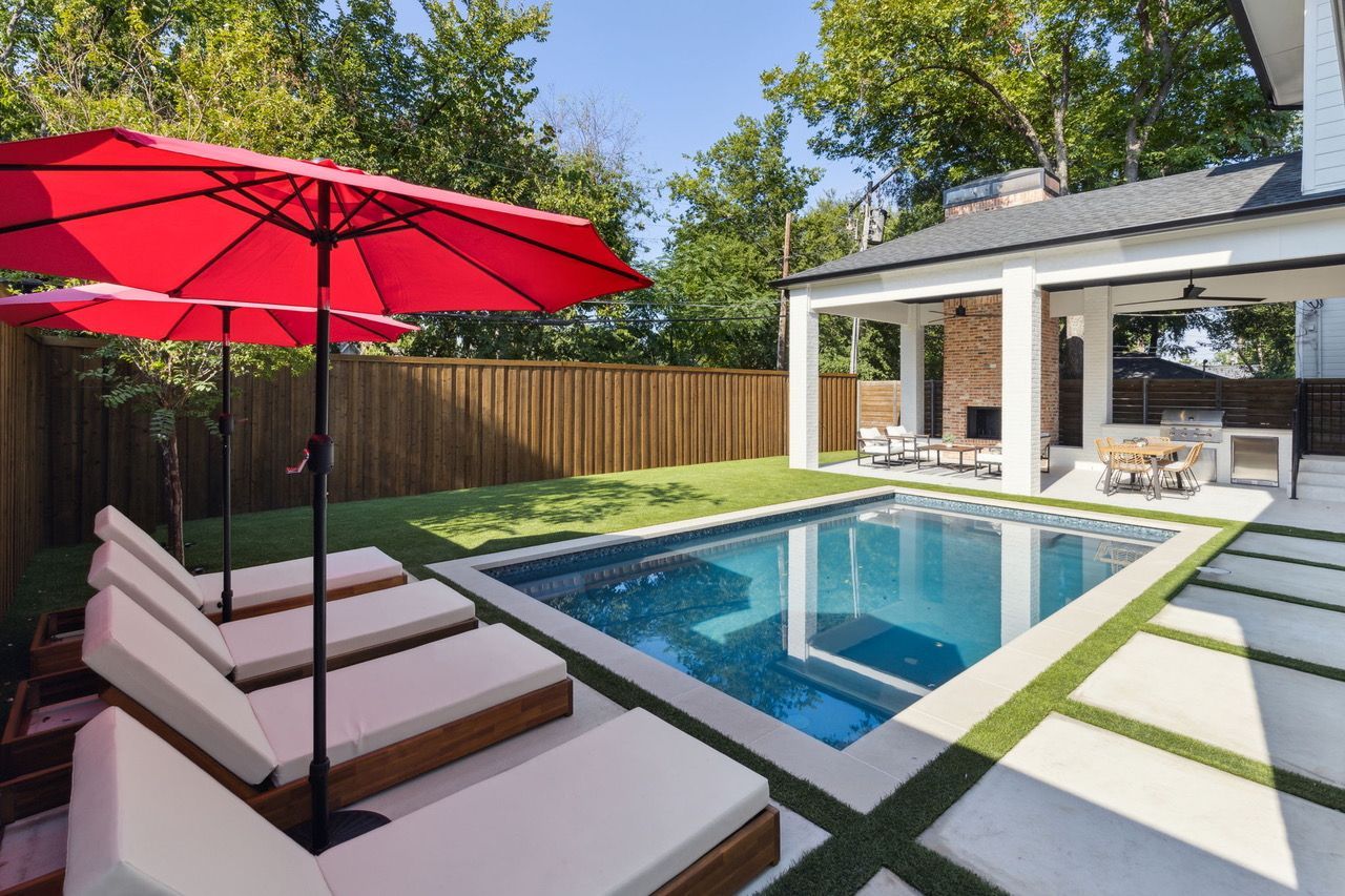 Backyard with pool, lounge chairs, red umbrellas, and outdoor kitchen.