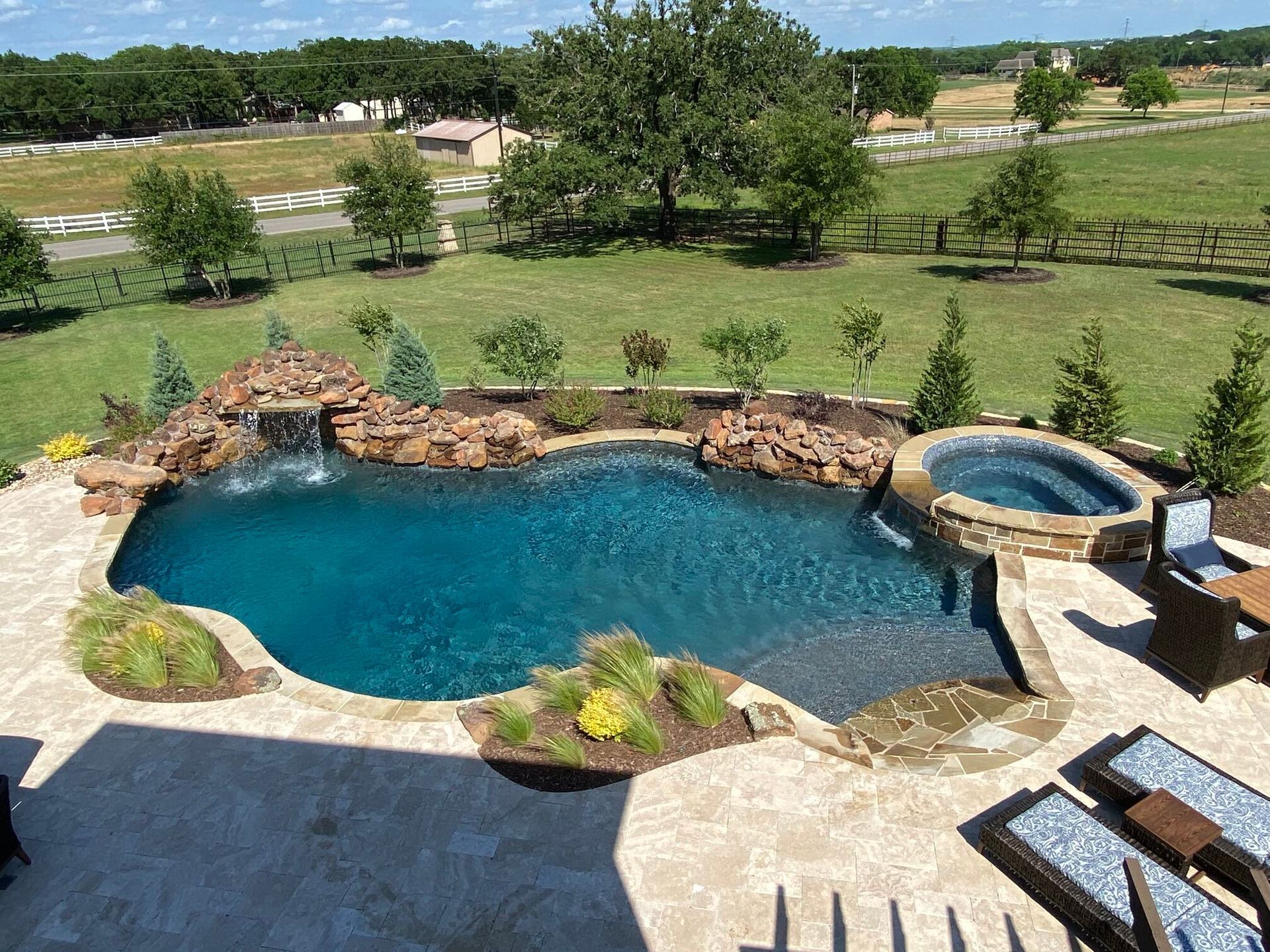 Pool with waterfall, spa, and patio overlooking a grassy yard.
