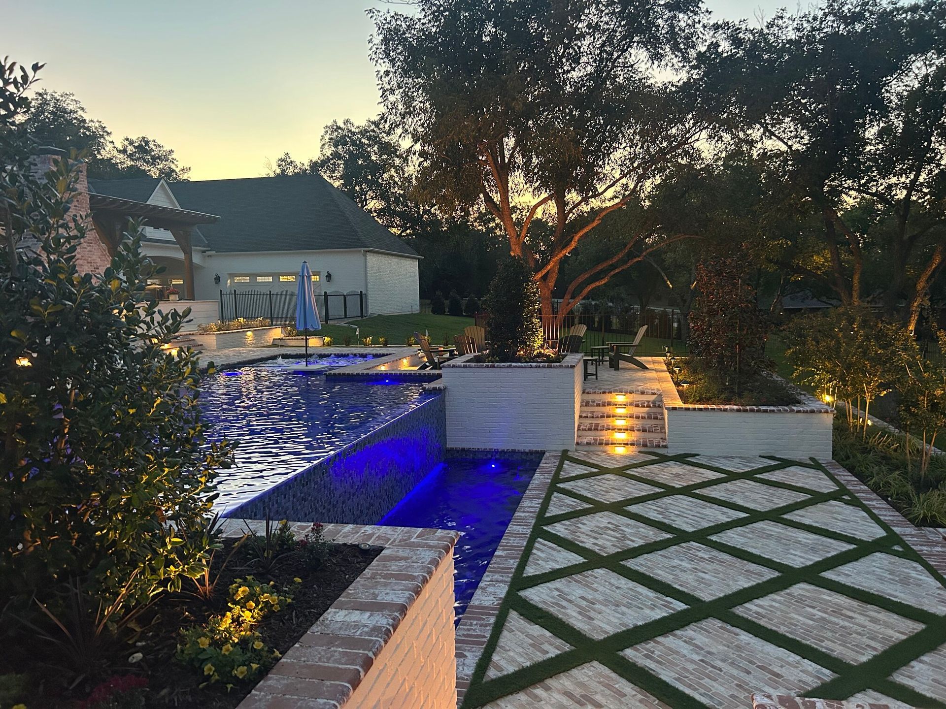 Backyard pool and patio with nighttime lighting near a house.