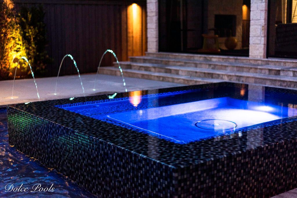 luxury pool with spout fountains and blue lights at night