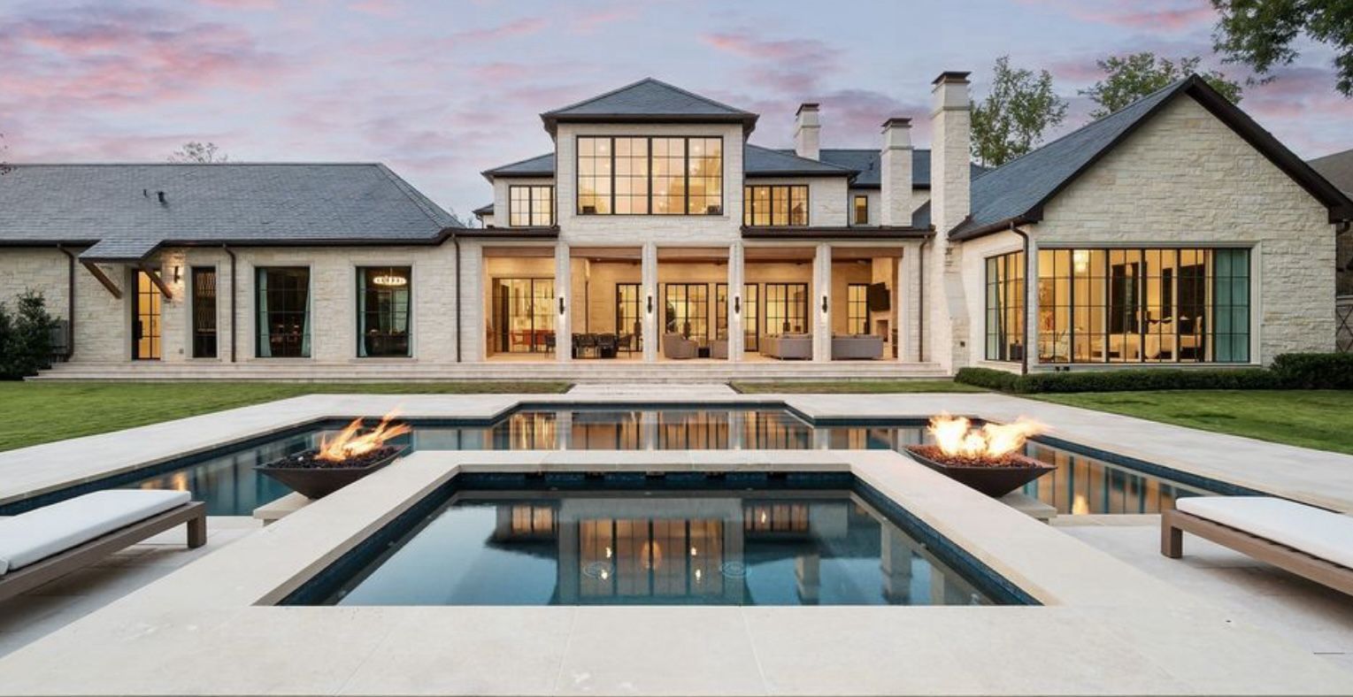 Luxury home exterior with a pool, fire features, and a sunset sky.