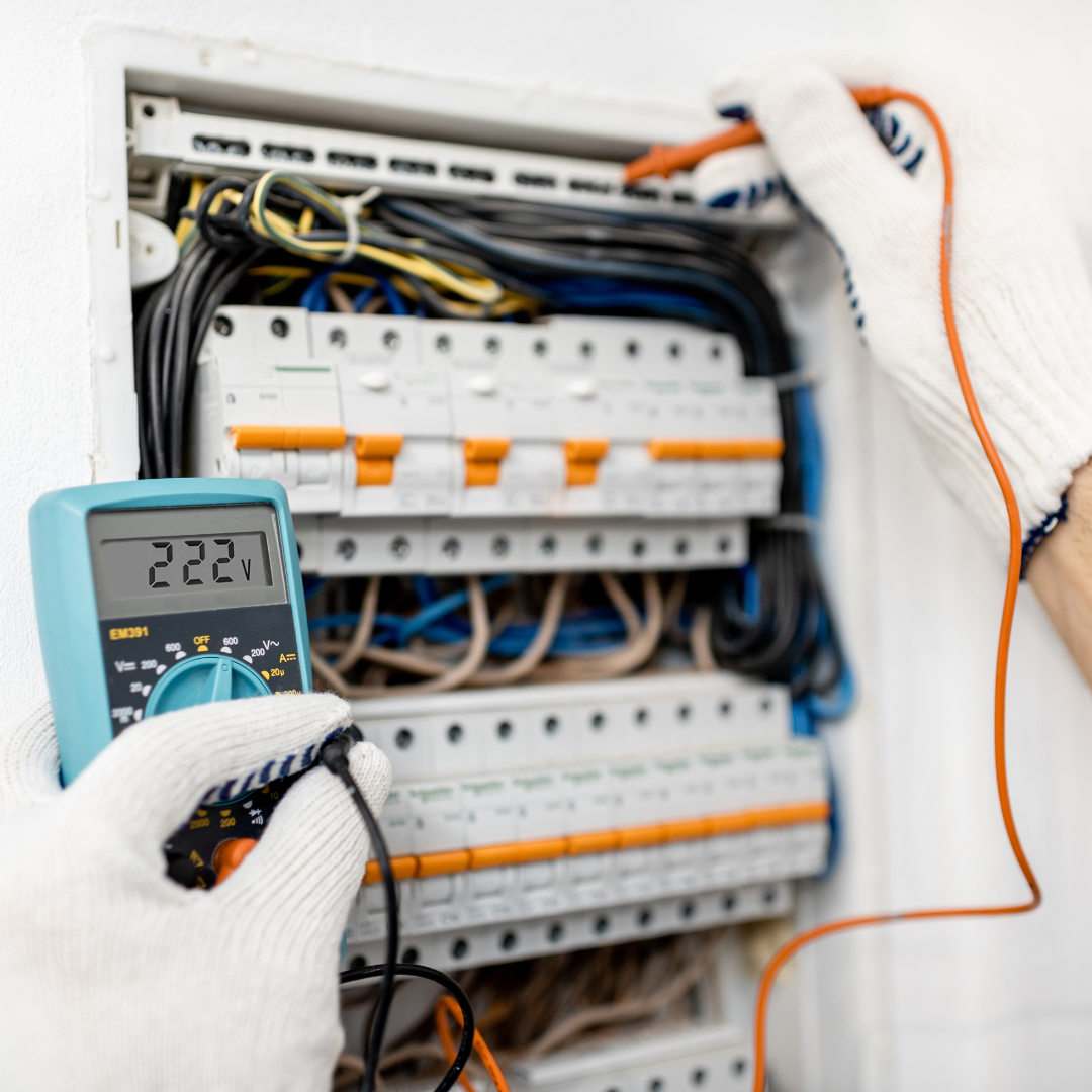 A person is holding a multimeter in front of an electrical box.