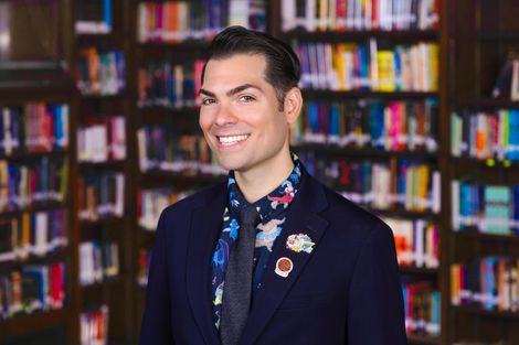 Photo of 40 year old Principal James Nicotri smiling with eyebrows that are arched, with a bookshelves in the background.