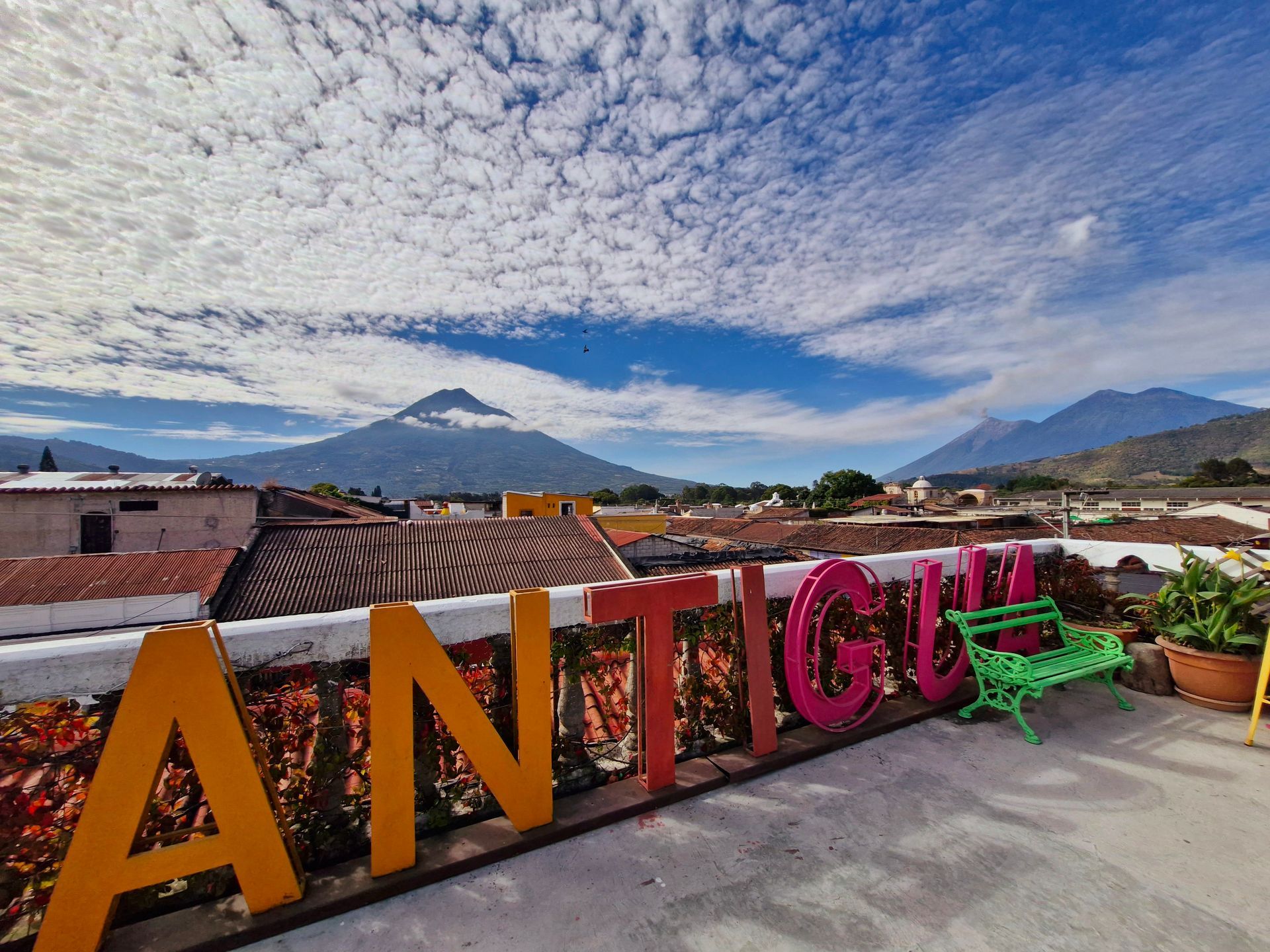 Un cartel que dice Antigua está en una azotea con montañas al fondo.