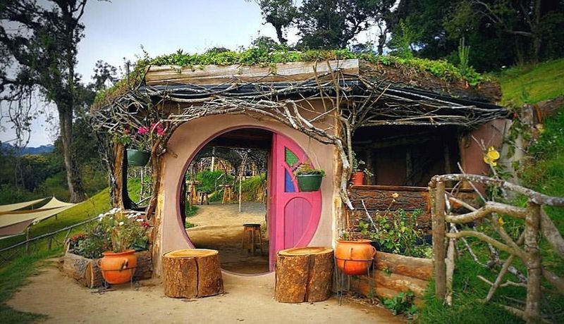 Una pequeña casa con una puerta rosa y taburetes delante de ella.