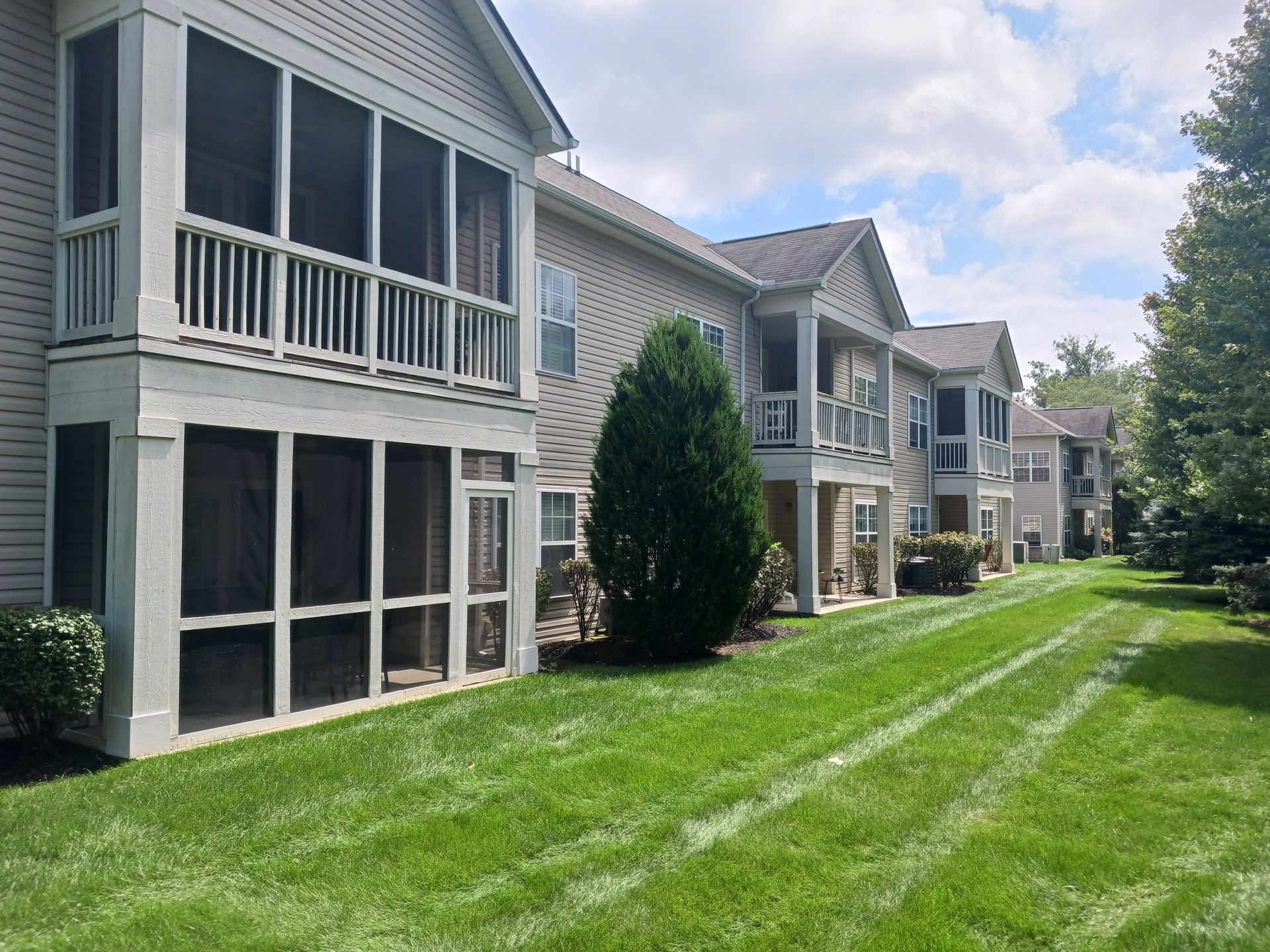 Row of tan townhouses with screened-in porches on a sunny day with green grass.