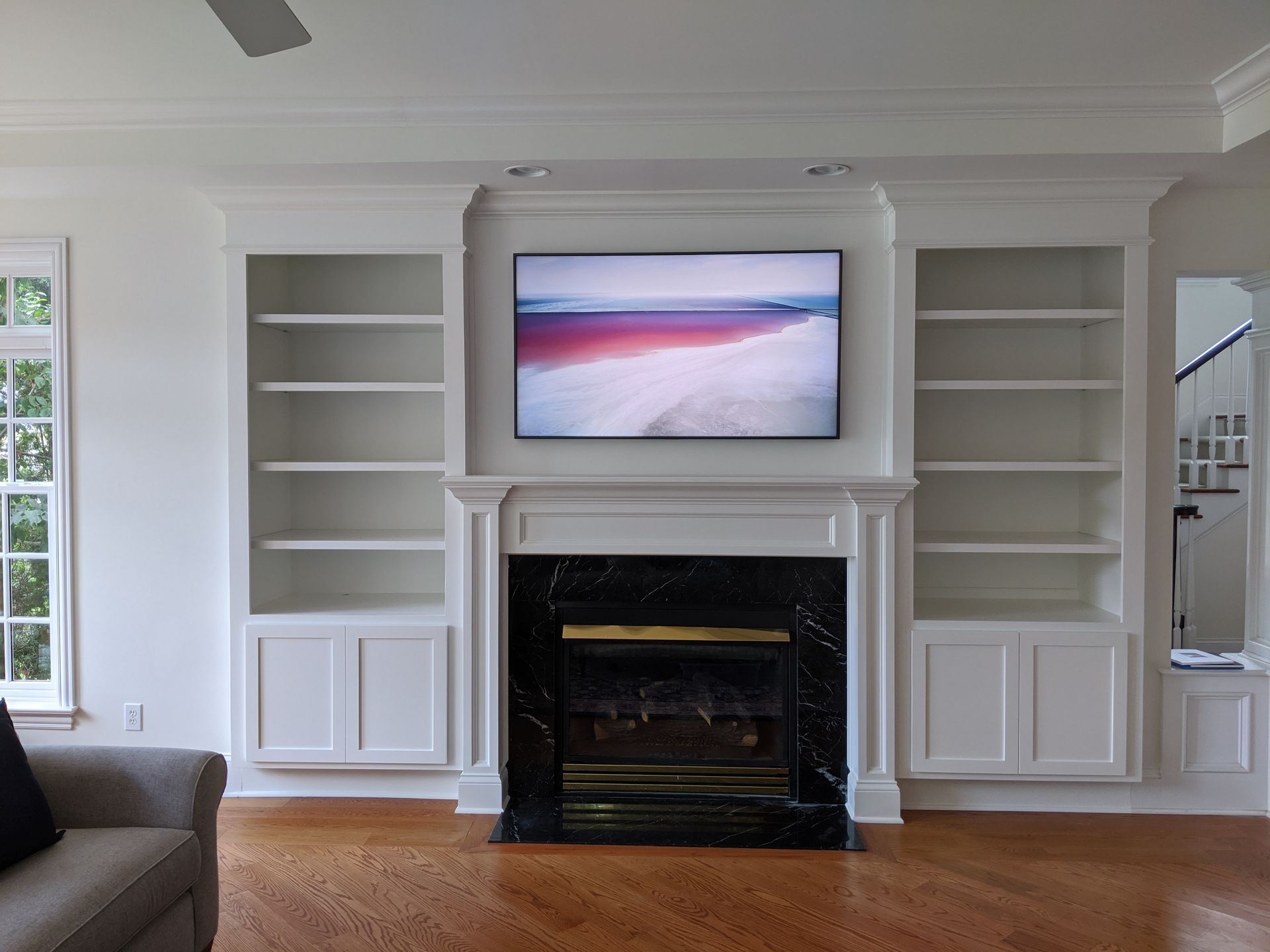 Built-in white bookshelves flank a fireplace with a TV above. The black marble fireplace has a lit gas fire.