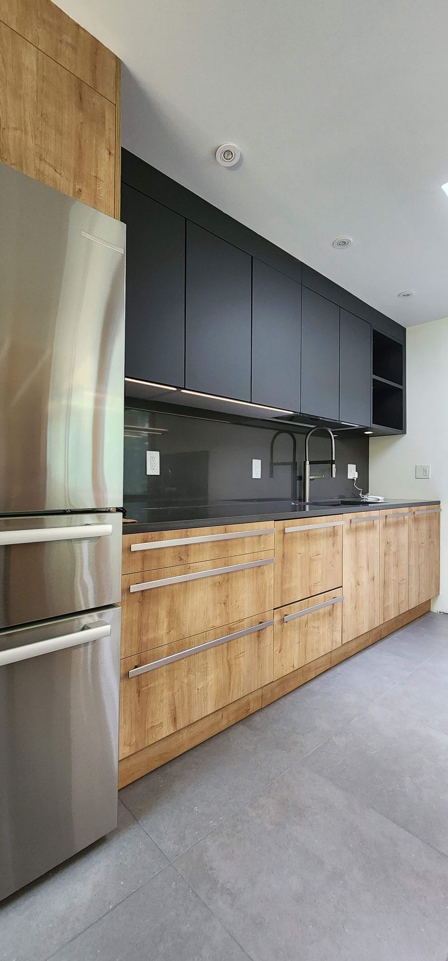 Modern kitchen with black upper cabinets, wooden lower cabinets, and stainless steel refrigerator.