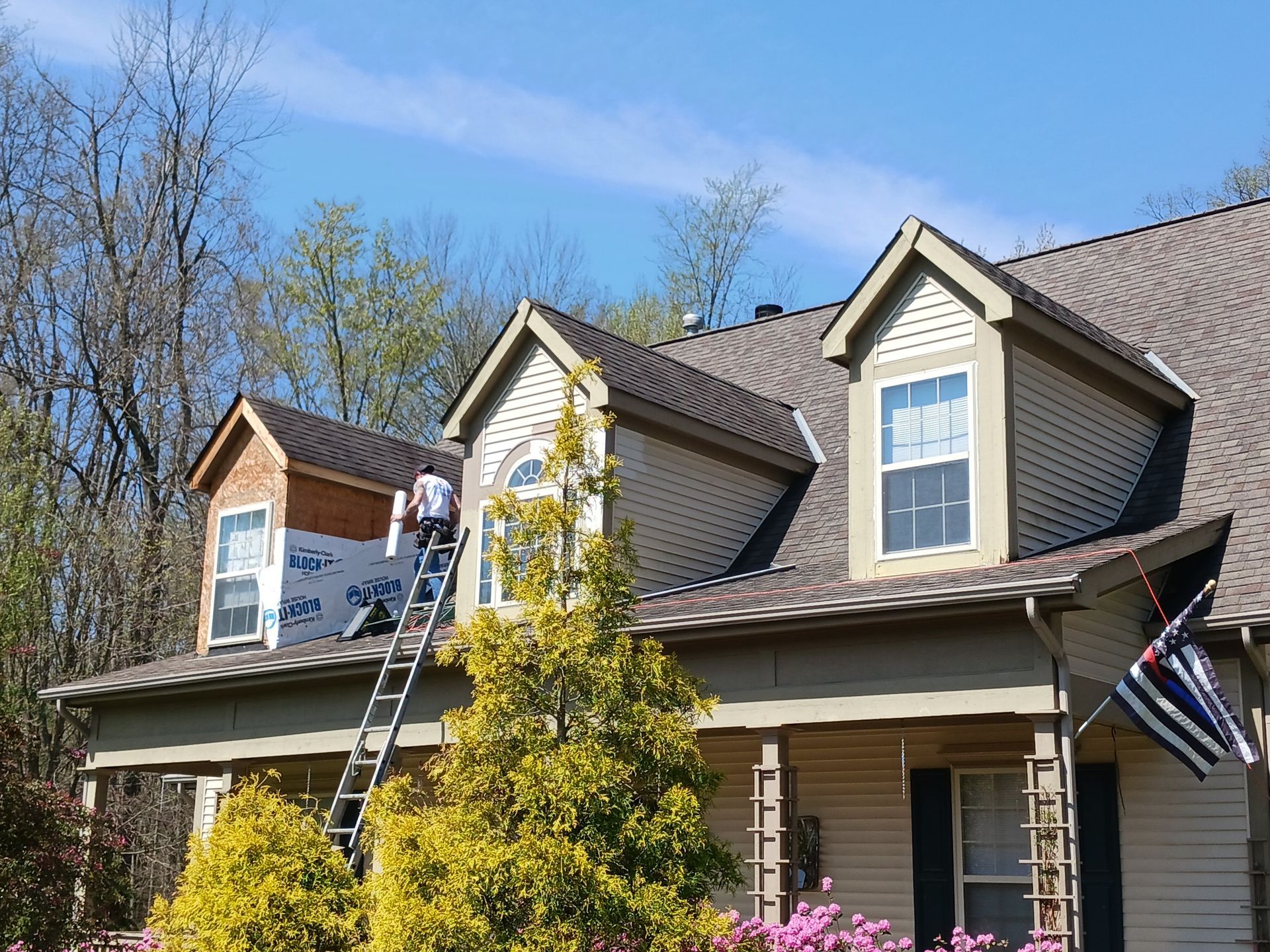 Man on ladder repairing roof with blue sky background.