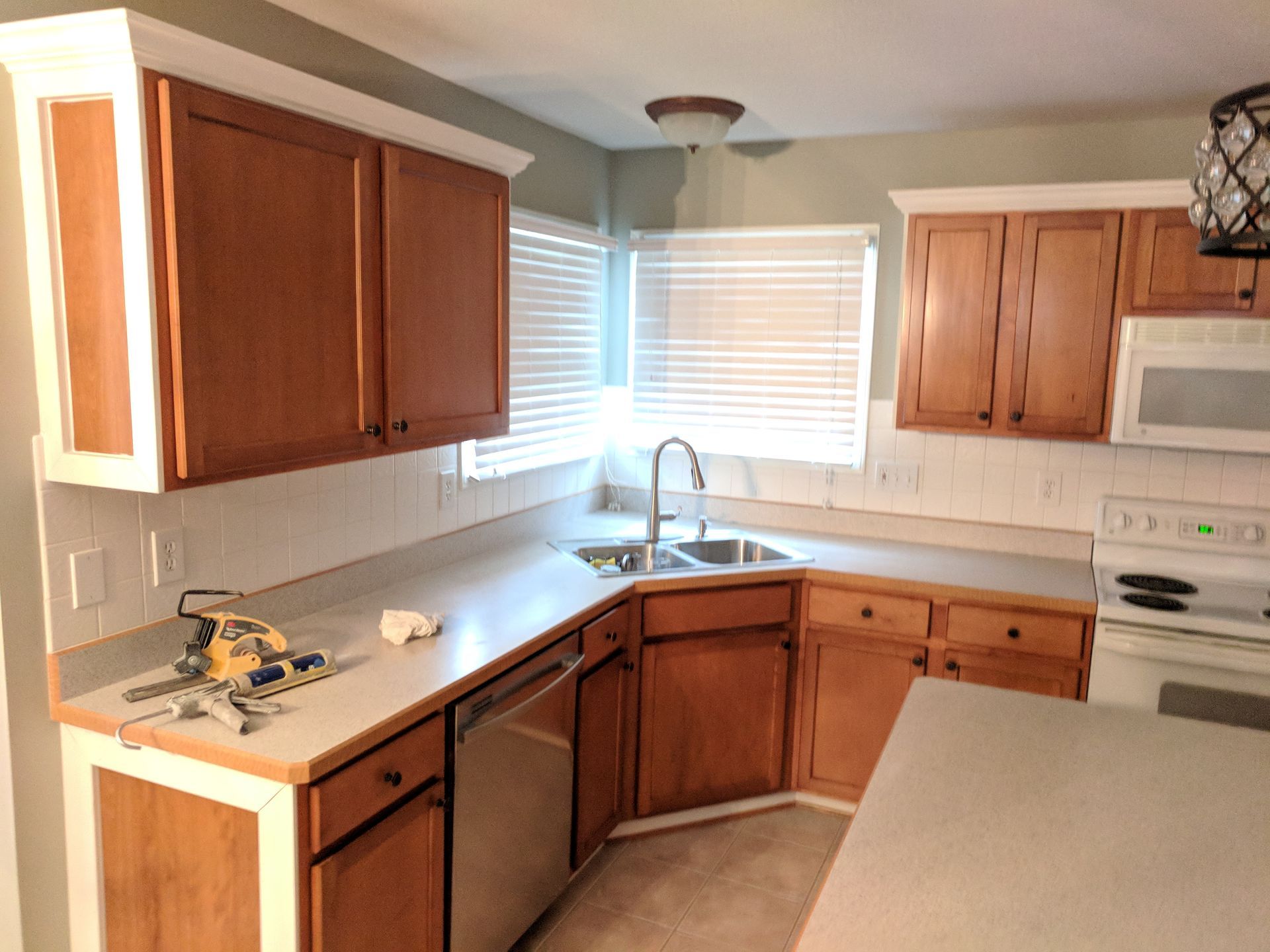 Kitchen with light countertops and wooden cabinets, some with white trim. A window sits above the sink, with a microwave and stove nearby.