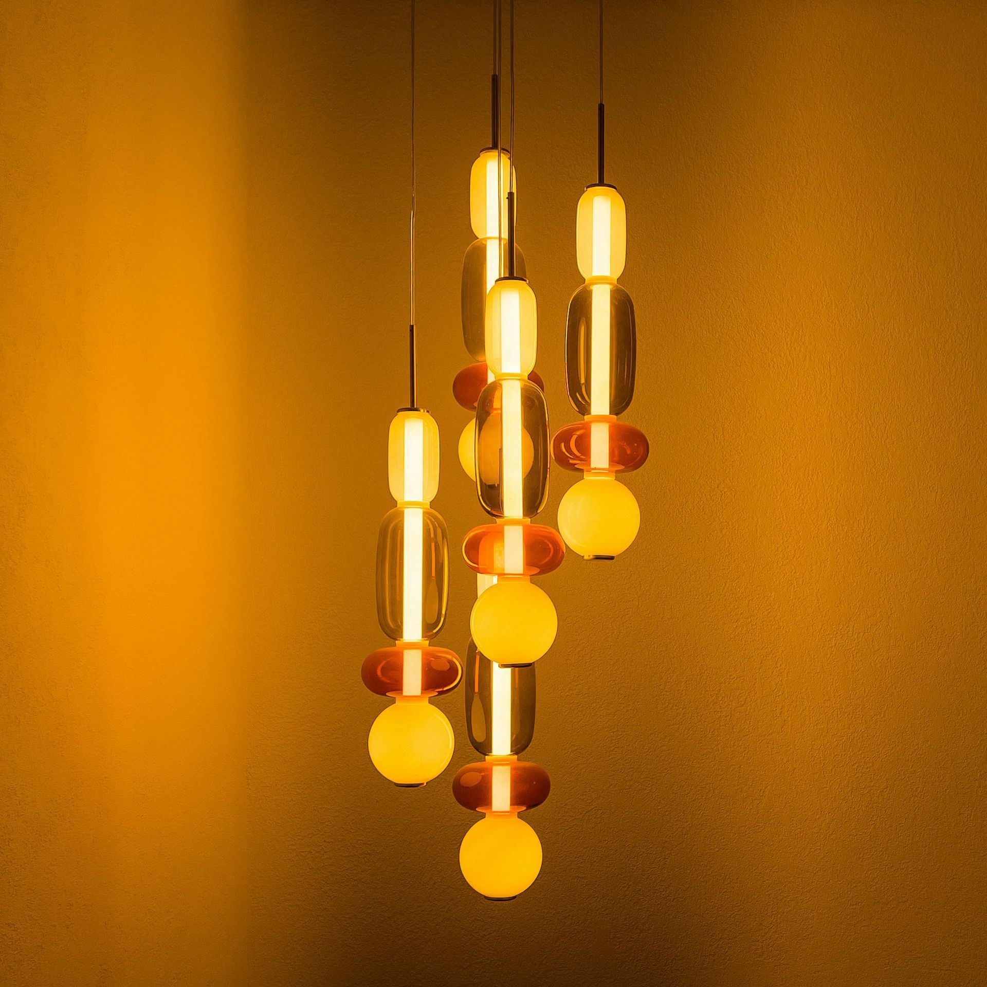 A cluster of pendant lights hanging from the ceiling against a yellow wall.
