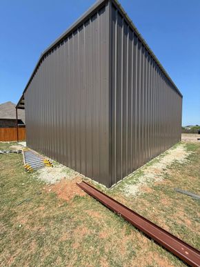 Gray metal shed with a pitched roof beside a grassy yard on a sunny day