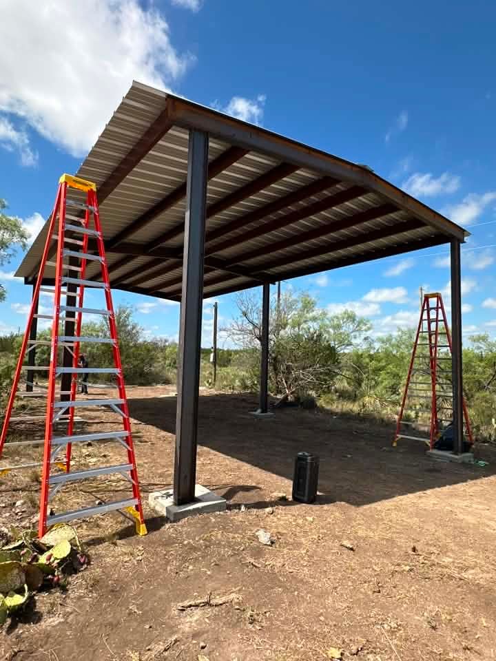 Partially built metal-roof shelter with ladders, on a dirt site under a blue sky