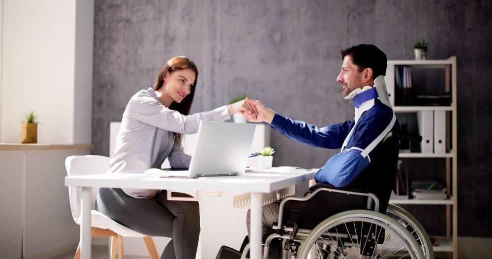 A man in a wheelchair is shaking hands with a woman at a desk.