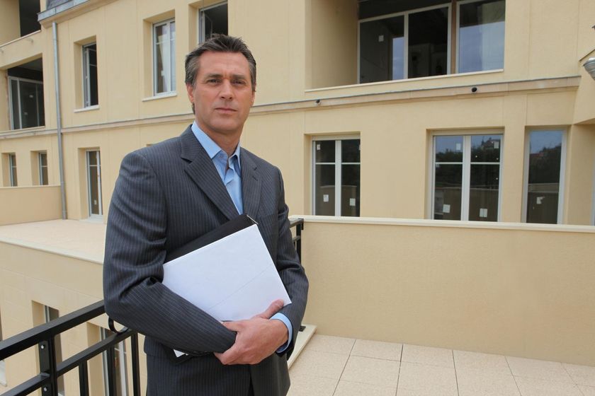 A man in a suit holds a piece of paper in front of a building