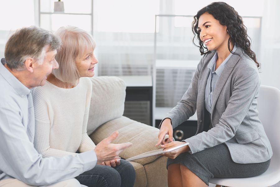 An elderly couple is sitting on a couch talking to a woman.