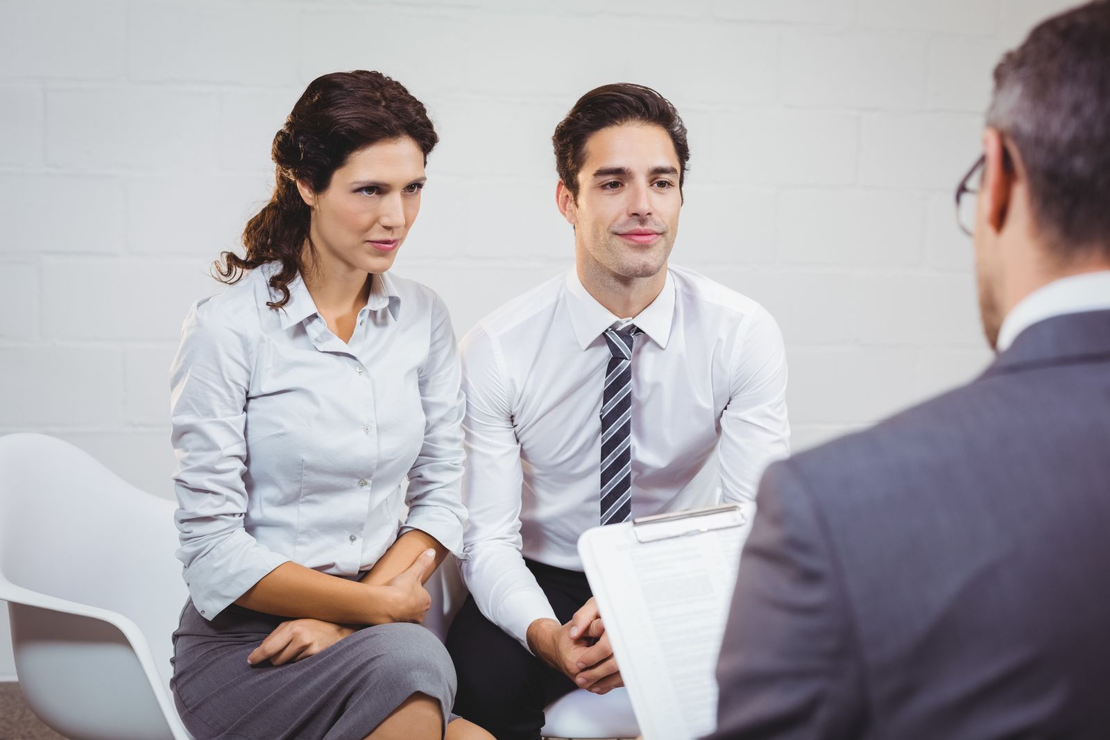 A man and a woman are sitting in chairs talking to a man in a suit.
