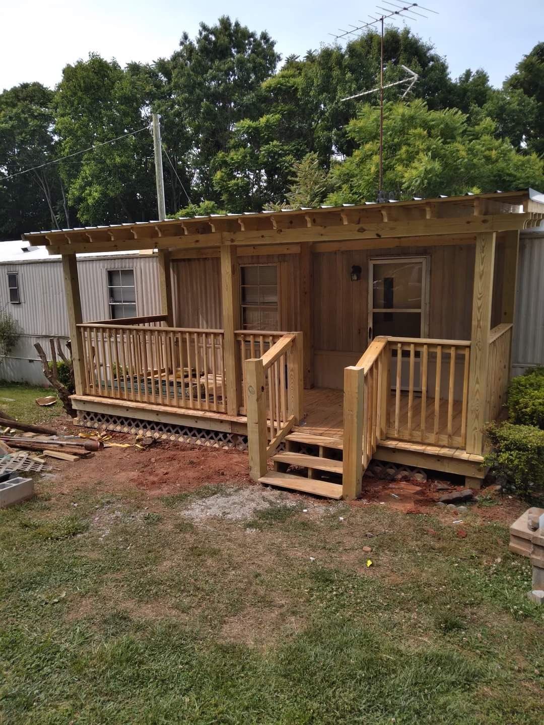 A person works on the wood-framed roof of a house addition under construction, with a yellow piece of equipment nearby.