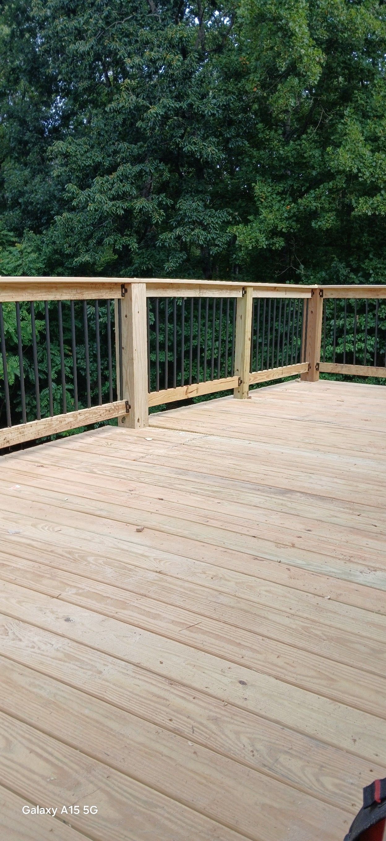 A paintbrush and a small bucket of dark wood stain sit on a wooden deck, partially stained a reddish-brown color.