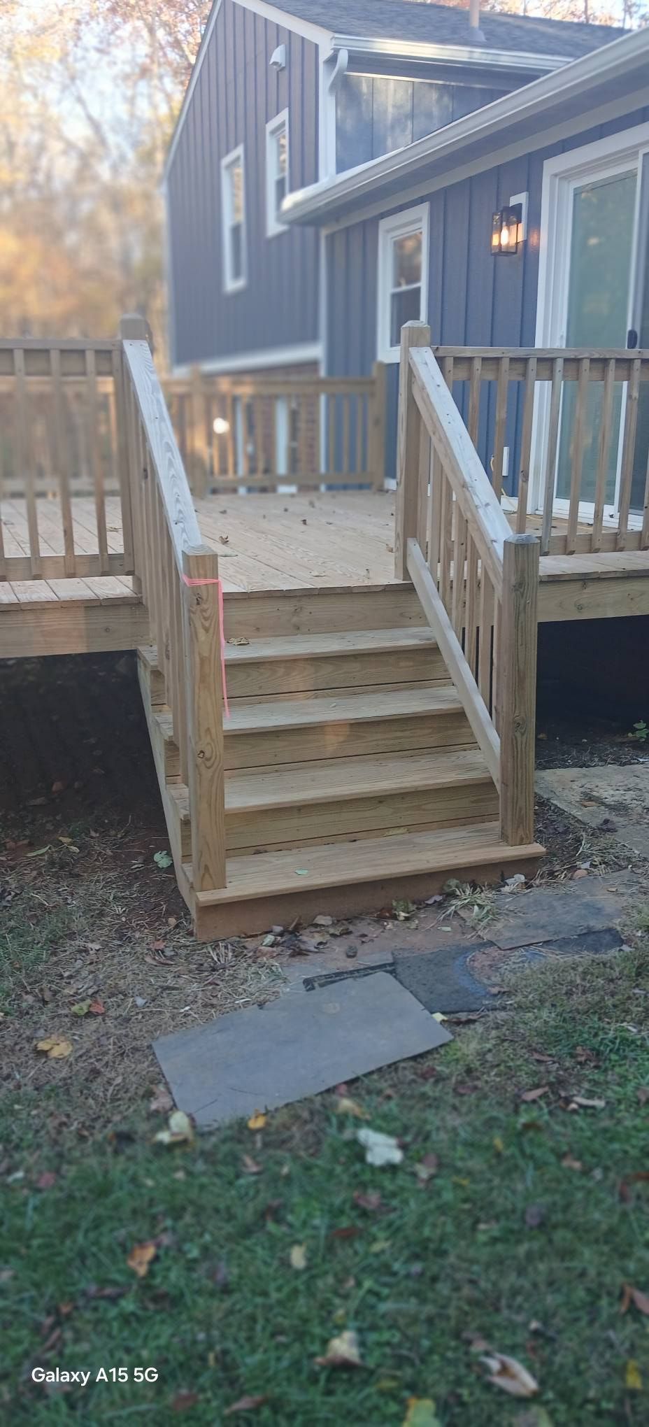 A wooden deck features a newly constructed pergola with a translucent corrugated plastic roof under a clear blue sky.