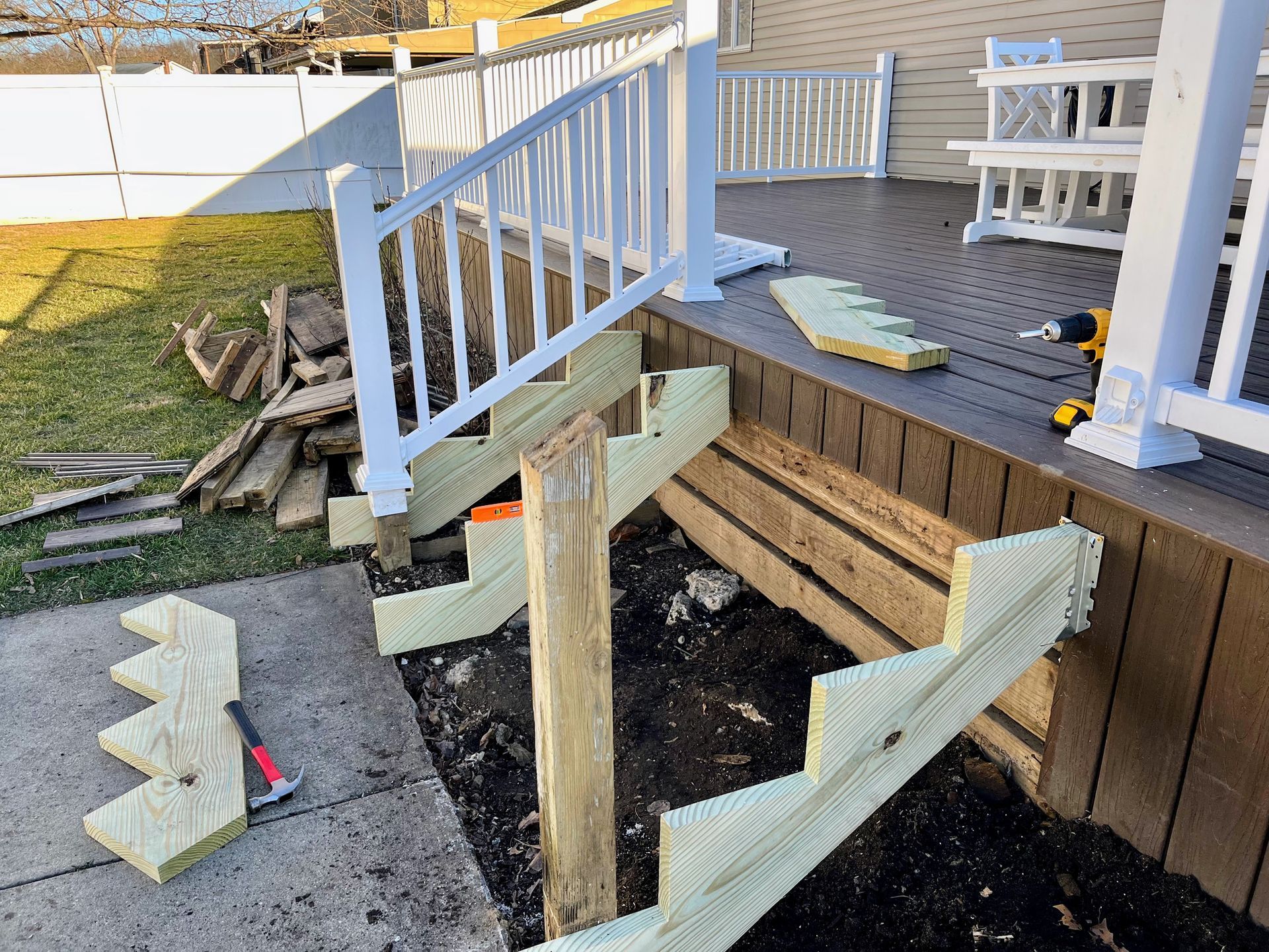 A partially built wooden deck staircase with green pressure-treated stringers under construction next to a house.