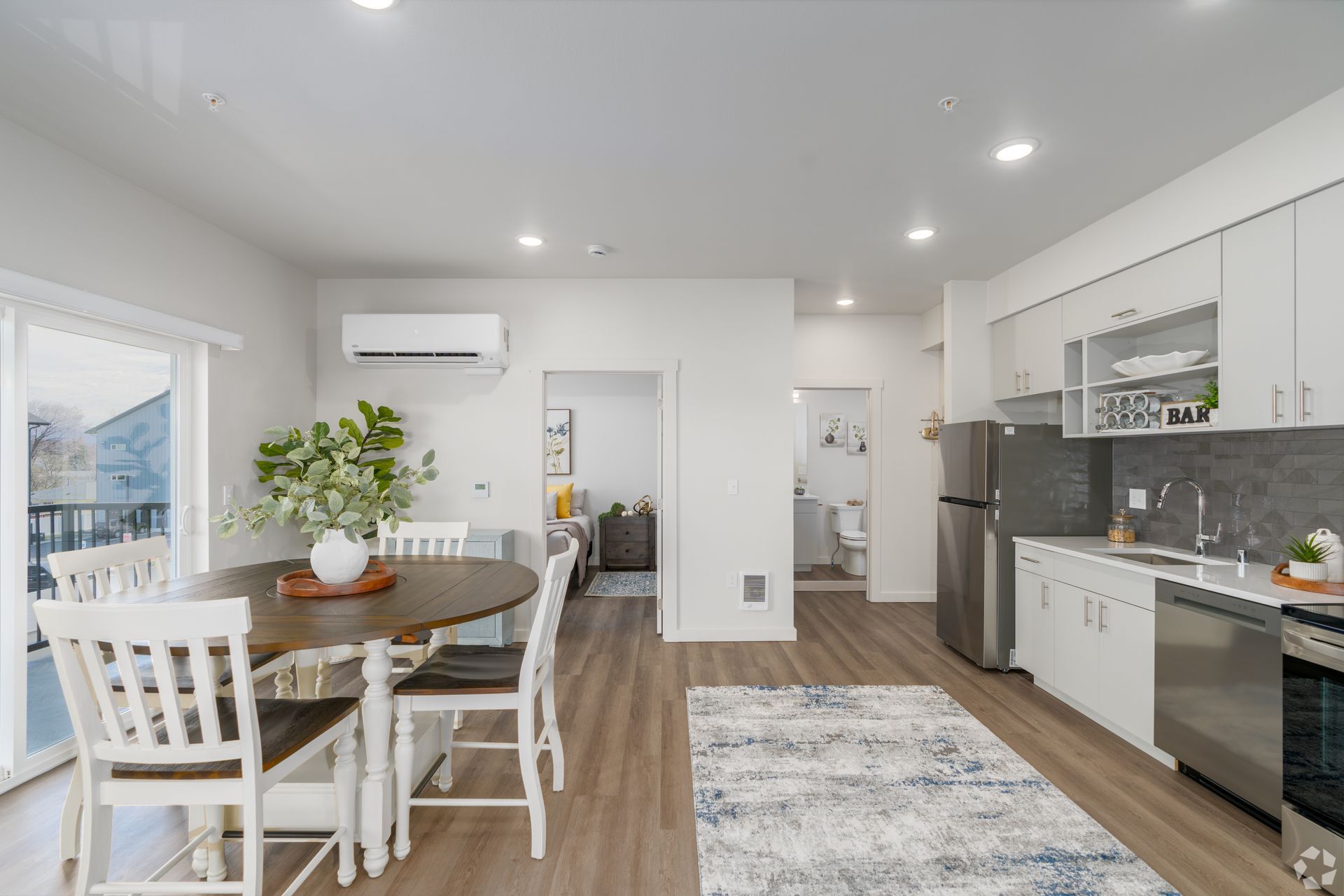 A living room with a dining table and chairs and a kitchen with stainless steel appliances.