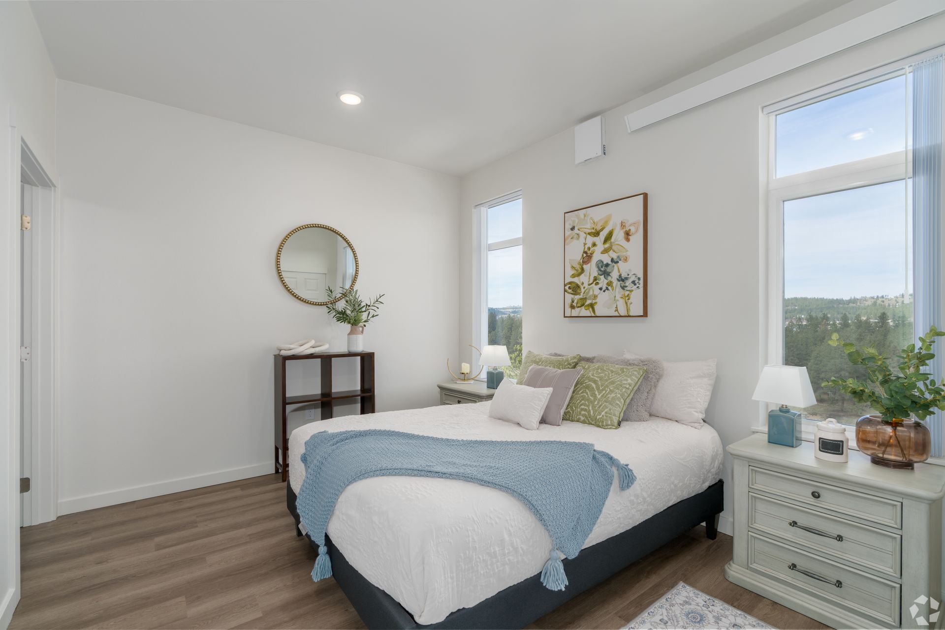 A bedroom with a bed , nightstand , mirror and window.