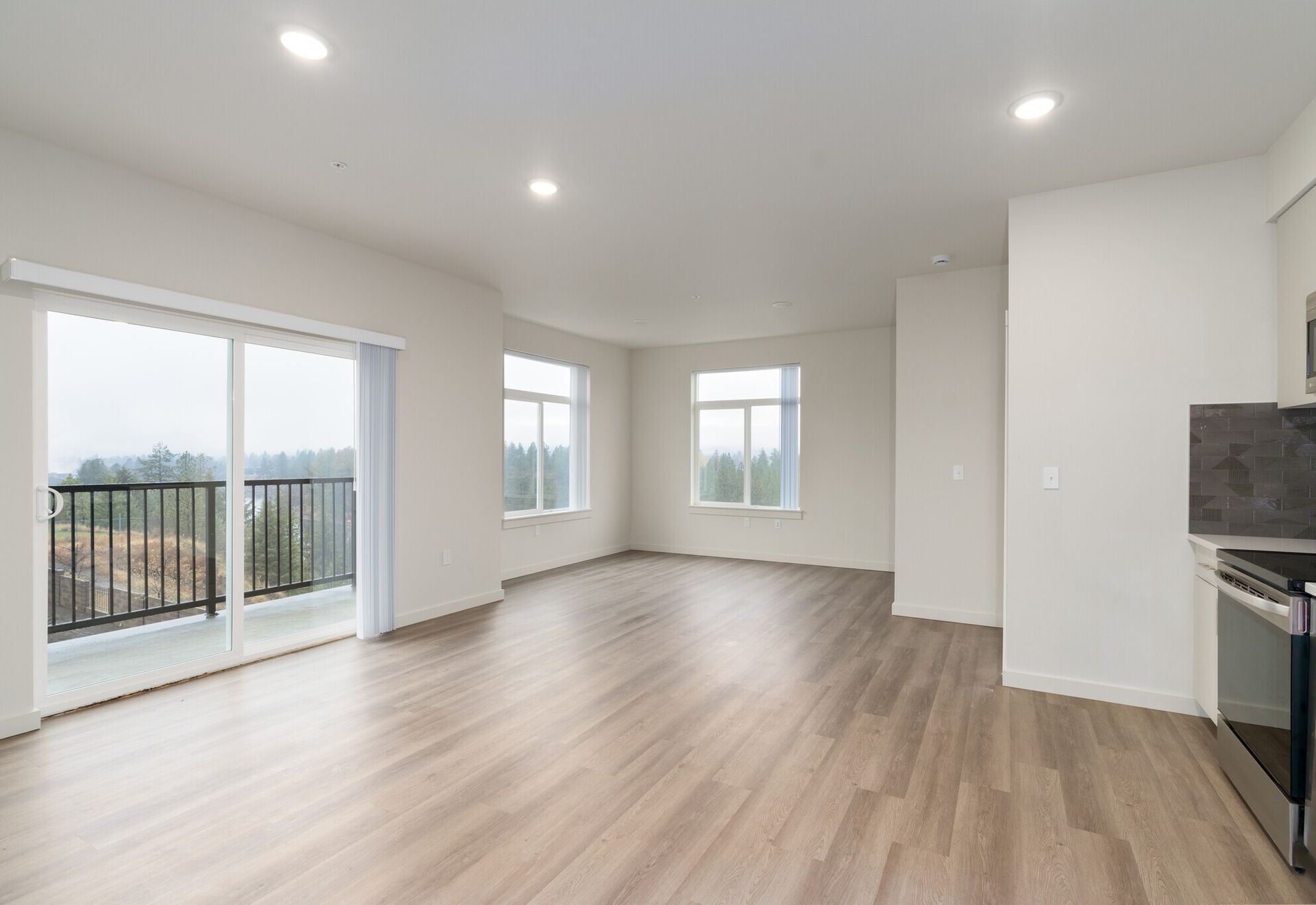 An empty living room with hardwood floors and sliding glass doors leading to a balcony.