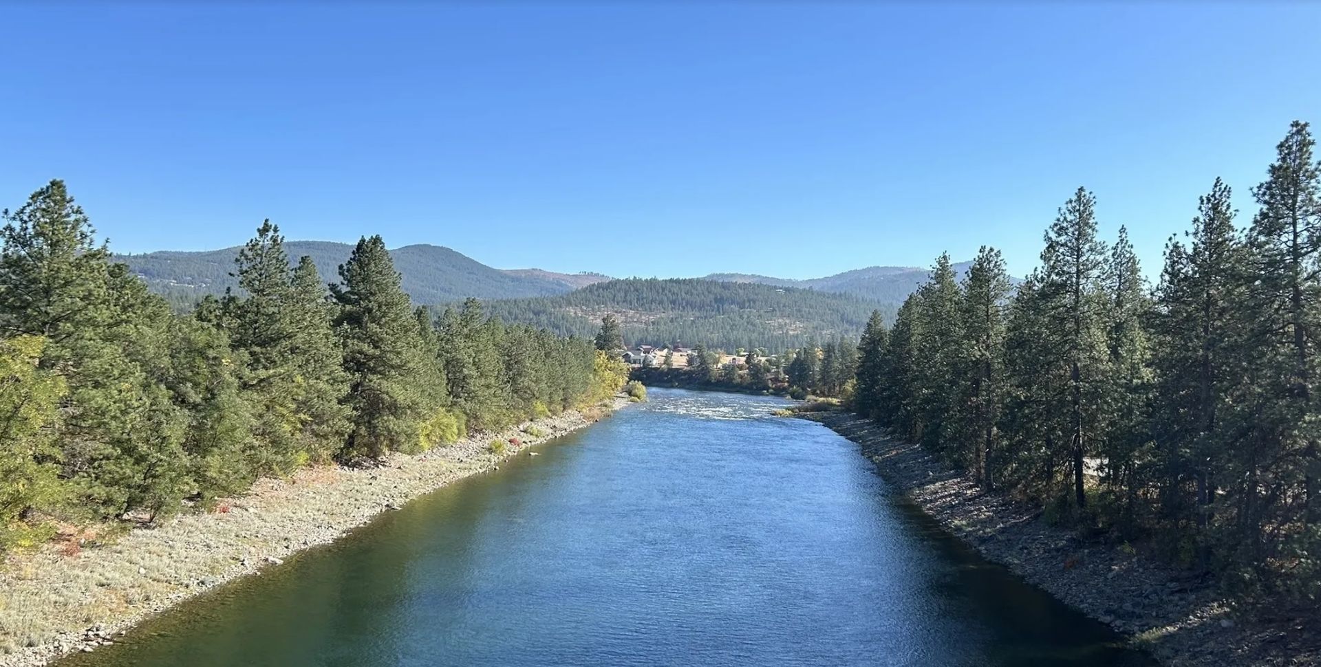 A river surrounded by trees and mountains on a sunny day.