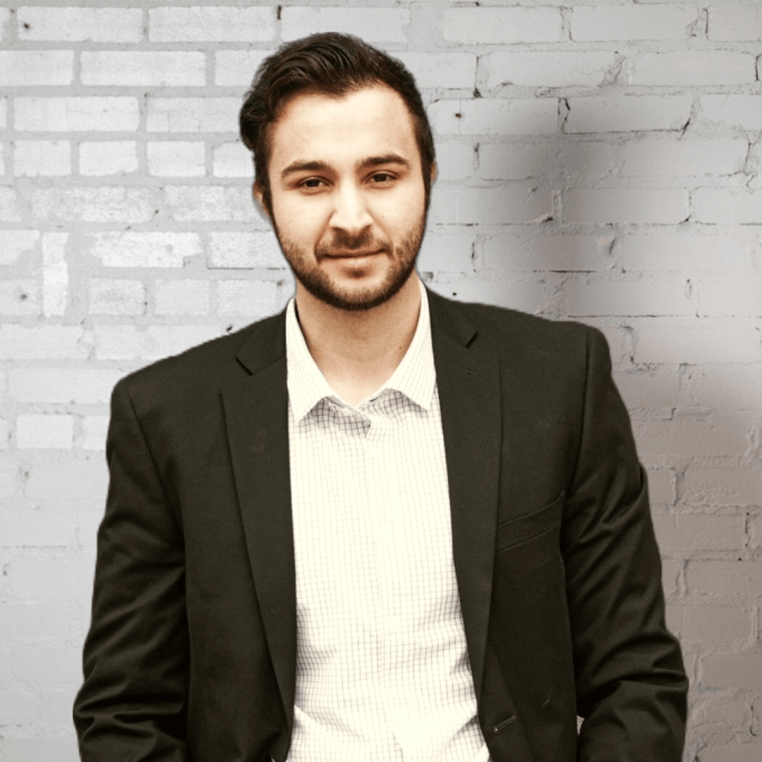 Omar Jebbeh in a suit is standing in front of a brick wall