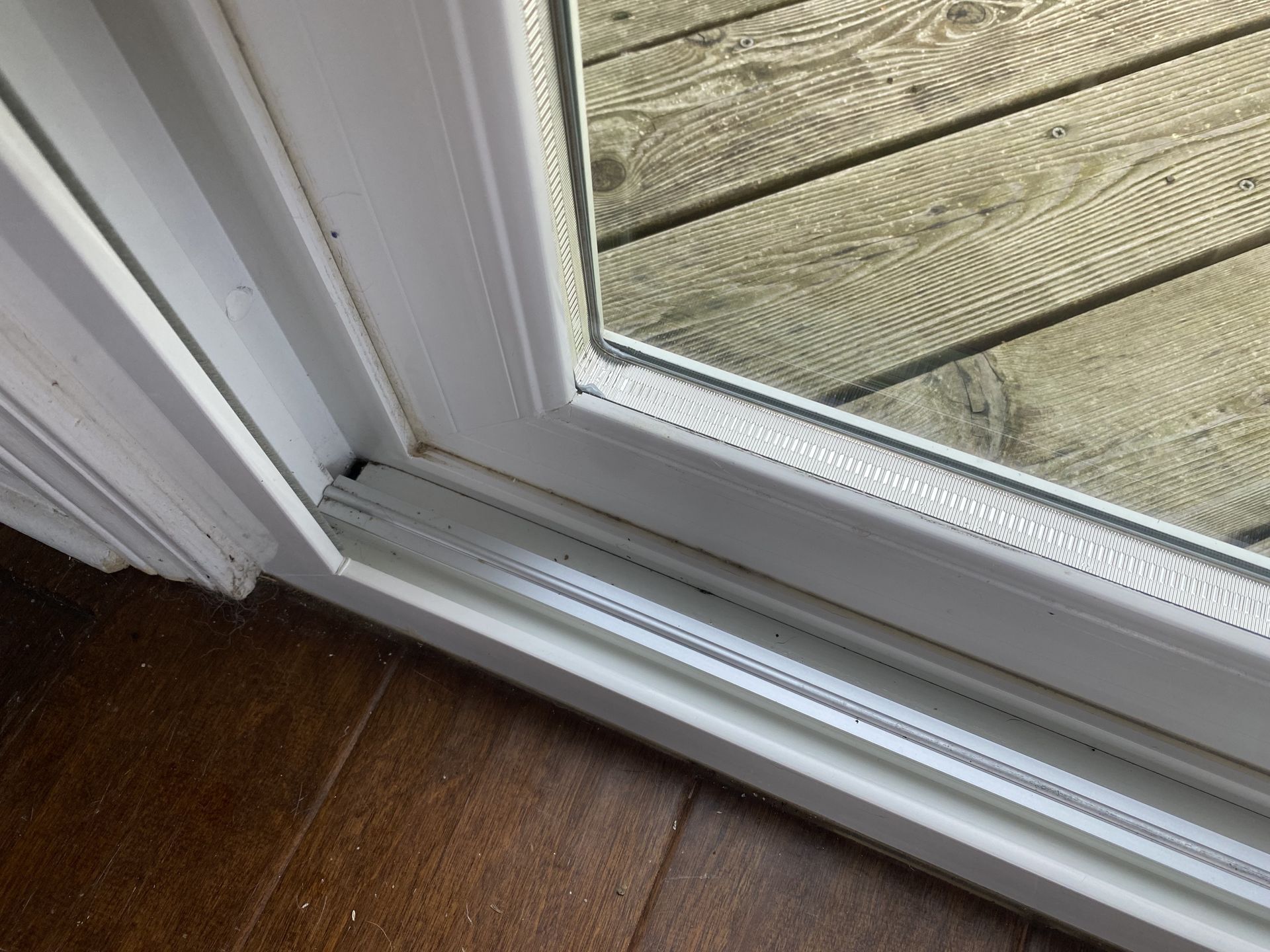 a white sliding glass door is open to a wooden deck .