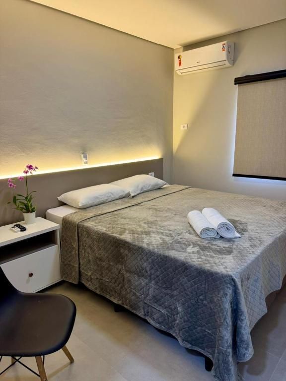 Um quarto com uma cama com colcha cinza estampada, travesseiros brancos, uma mesa de cabeceira branca e um ar-condicionado de parede.