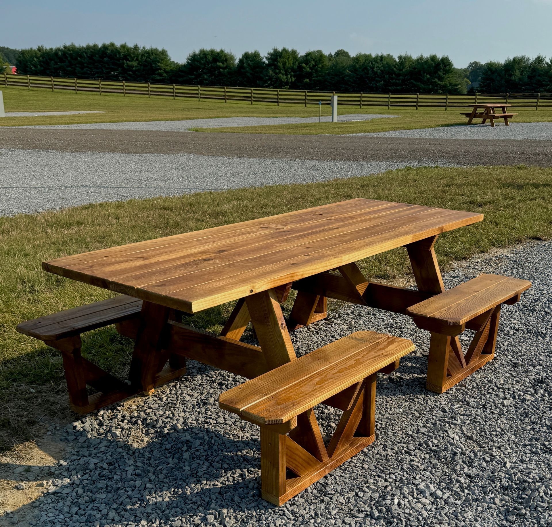 A wooden picnic table with two benches in a gravel area