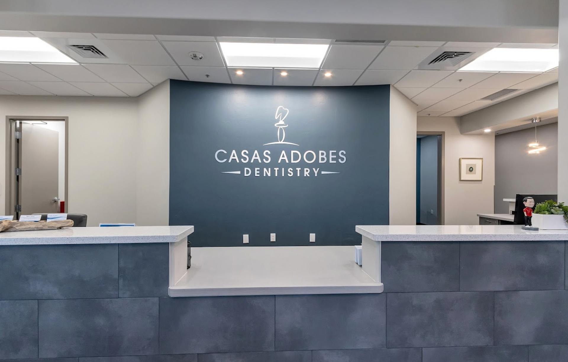 The front desk of a dental office with a sign on the wall that says casas adobes dentistry.