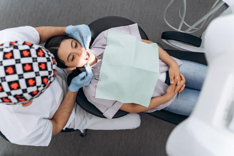 A woman is laying in a dental chair while a dentist examines her teeth.