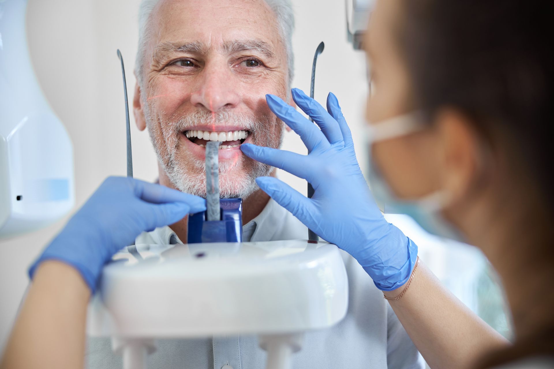 A dental professional wearing blue gloves holds a shade guide to a patient’s teeth to match their natural tooth color.