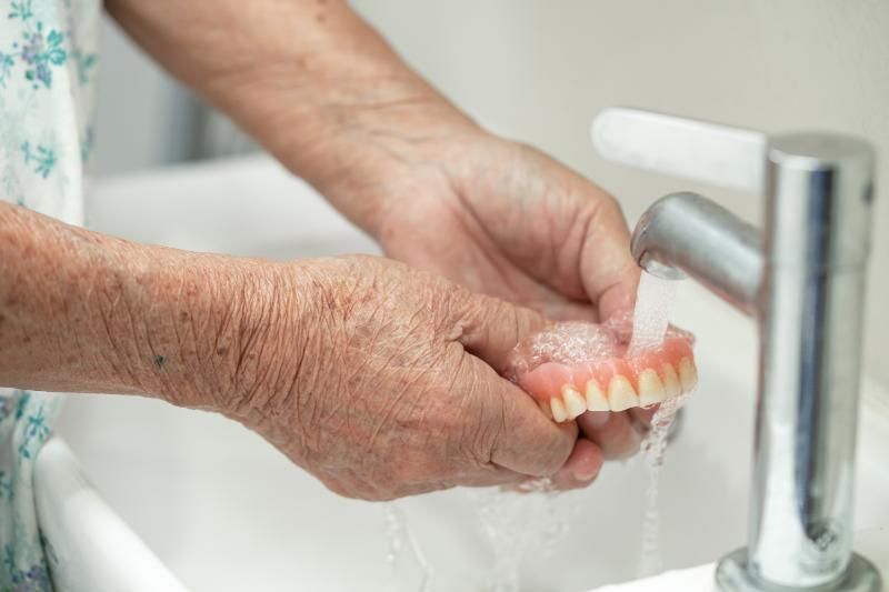 An elderly woman is washing her dentures in a sink.