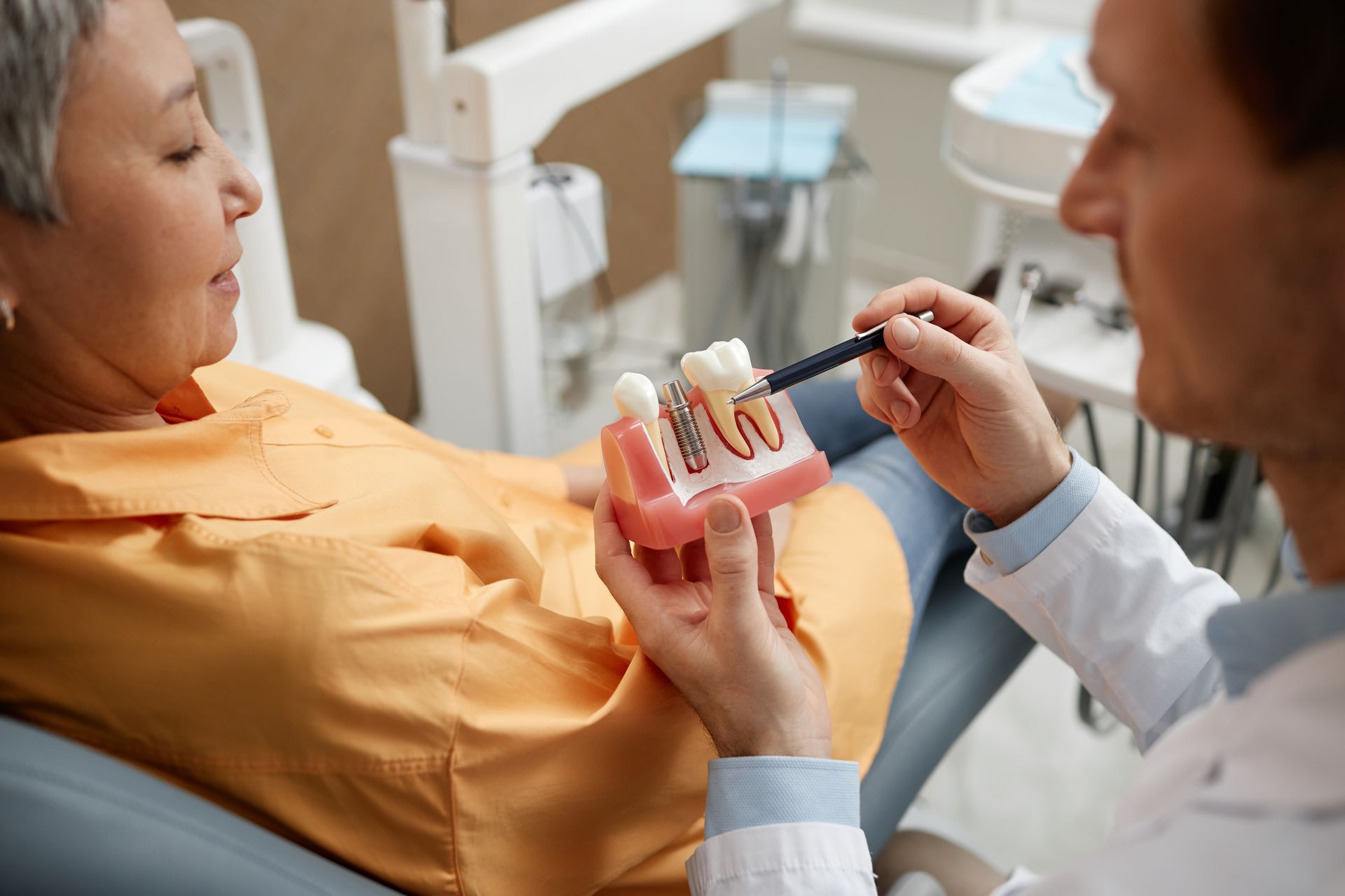 Dentist showing patient a model of teeth, explaining dental procedure.