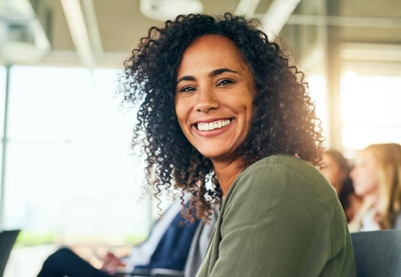 A woman with curly hair is smiling while sitting in a chair.