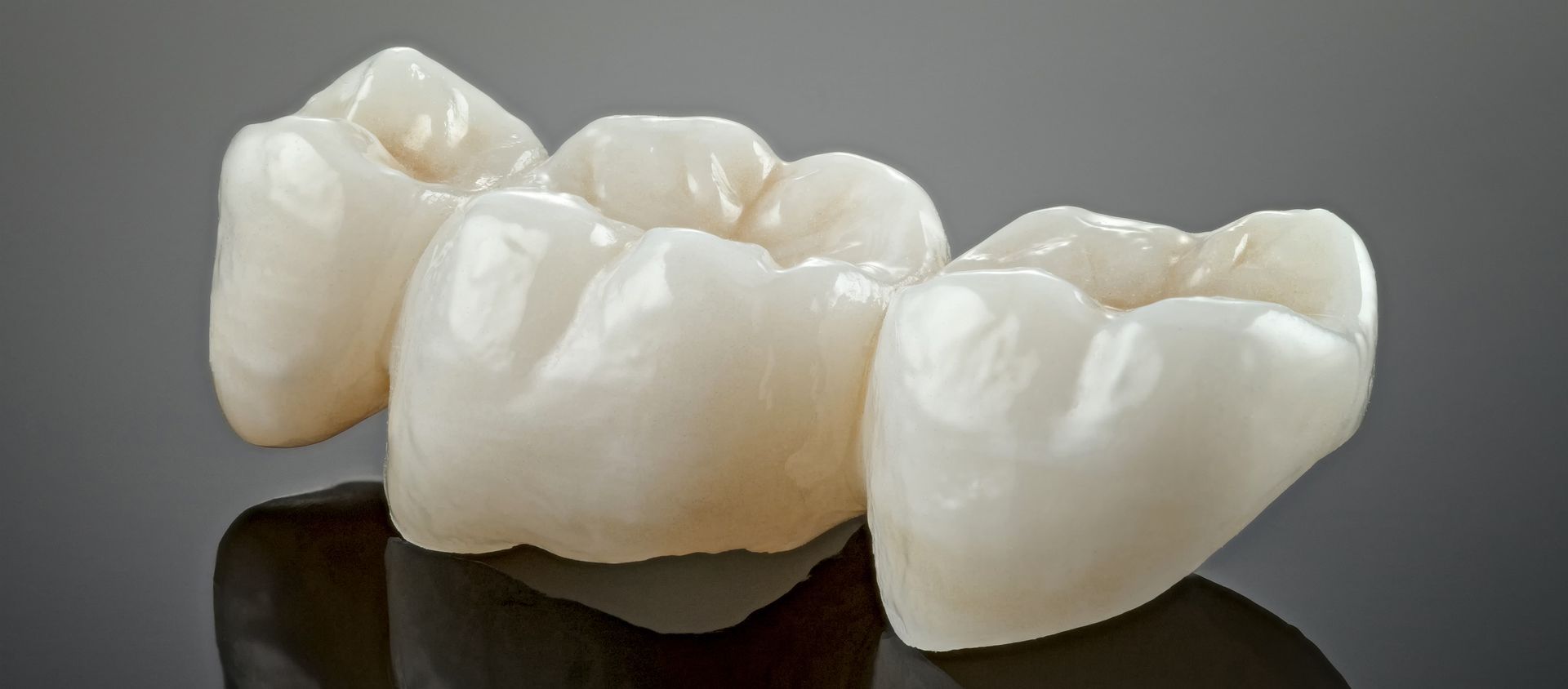 Three white dental crowns on a dark reflective surface